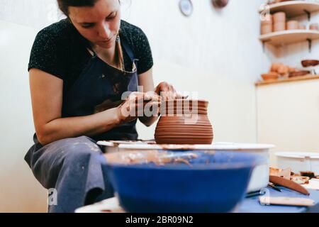 Frau ist von der Töpferei engagiert. Potter hinter dem Töpferrad bildet Ton, um Keramikschalen zu kreieren Stockfoto