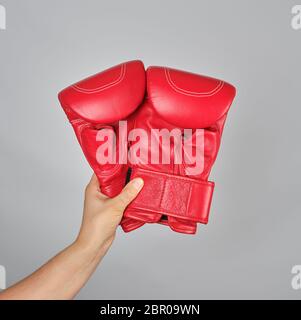 Paar rote Leder Boxhandschuhe in weiblicher Hand, grauer Hintergrund Stockfoto