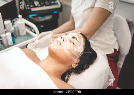 Der Kosmetologe wäscht die Maske vom Gesicht des Patienten ab. Entfernen einer Feuchtigkeitsmaske aus dem Gesicht Stockfoto