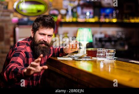 Betrunken und entspannt Konzept. Mann mit betrunkenem Gesicht sitzen alleine in der Bar oder im Pub neben der Theke. Guy verbringen Freizeit in der Bar, defokussed Hintergrund. Hipster hält Glas mit Whiskey oder alkoholischem Getränk. Stockfoto