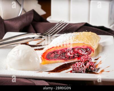 Süße Nachspeise - Strudel mit Kirschen und auf weiße Platte mit Eis am Tisch im Restaurant Stockfoto