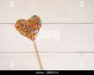 Candy besprüht Form Herz Form. Bunte Herz-Form von candy Konfetti auf weißem Holz- Hintergrund. Valentines Tag Konzept. Ansicht von oben oder Wohnung La Stockfoto