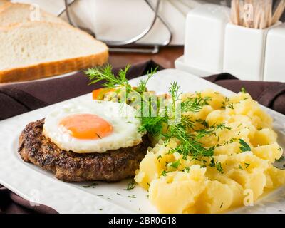 Beefsteak mit Spiegelei und Kartoffelpüree auf weiße Platte close-up auf dunkelbraunen hölzernen Tisch im Restaurant Stockfoto