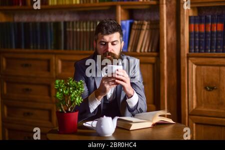 Mann mit ruhigem Gesicht genießt heißes Getränk. Businessman sitzt in luxuriösem Interieur und hält eine Tasse Tee. Bärtiger Mann in elegantem Anzug in seinem Schrank. Englischer Tee, britischer Lebensstil, Erfolg, Tee-Zeit-Konzept. Stockfoto