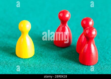 Konzept-Szene - eine gelbe Spielfigur vor drei rote Spielfiguren auf grünem Filz Tisch Stockfoto