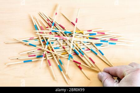 Spieler nimmt einen Stick von Stapel in Mikado Spiel auf Holzbrett Stockfoto