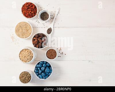 Verschiedene Superfoods in kleiner Schüssel auf weißem Holztisch.Auswahl Superfood.Superfood als Heidelbeere, Chia, rohe Kakaobohne, Goji, Hanfsamen, Quinoa, br Stockfoto