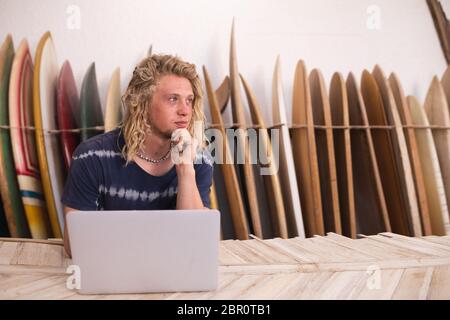 Kaukasischer Surfboard-Hersteller in seinem Studio, der mit Surfbrettern im Hintergrund arbeitet Stockfoto