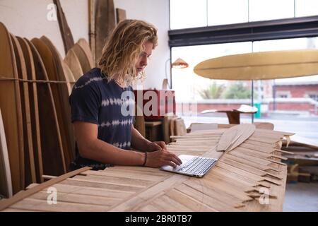 Kaukasischer Surfboard-Hersteller in seinem Studio, der mit Surfbrettern im Hintergrund arbeitet Stockfoto