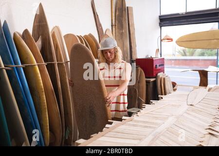 Kaukasischer männlicher Surfboard-Hersteller in seinem Studio, der eines der Surfbretter inspiziert Stockfoto