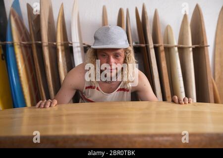 Kaukasischer männlicher Surfboard-Hersteller in seinem Studio, der eines der Surfbretter inspiziert Stockfoto