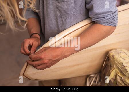 Kaukasischer männlicher Surfboard-Hersteller in seinem Studio, der einen Surfboard-Rand poliert Stockfoto