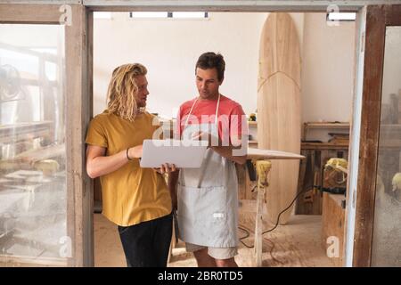 Zwei kaukasische männliche Surfboard-Hersteller stehen am Türrahmen und arbeiten an Projekten Stockfoto