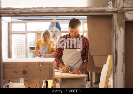 Zwei kaukasische männliche Surfboard Hersteller machen ein hölzernes Surfbrett zusammen und inspizieren es Stockfoto