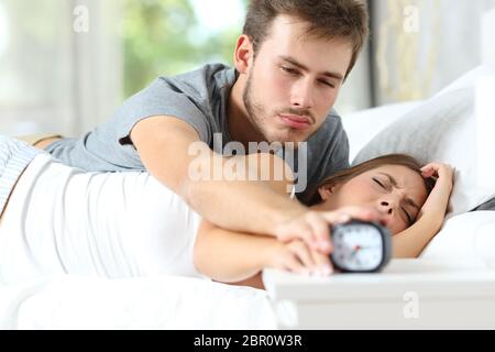 Sleepy paar Wachen ausschalten Wecker in das Bett am Morgen zu Hause liegen Stockfoto