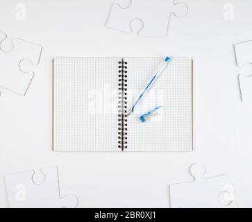 Öffnen Notebook in einer Zelle und einem blauen Stift auf weißem Hintergrund, neben große leere Rätsel, Ansicht von oben Stockfoto