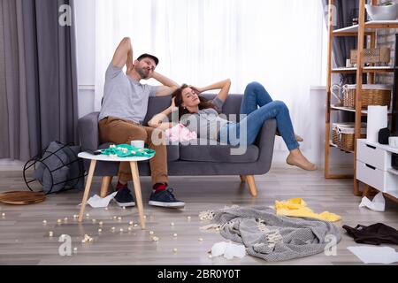 Lächelndes Paar entspannt auf einem Sofa im Wohnzimmer zu Hause unordentlich Stockfoto