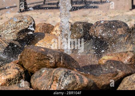 Nahaufwasserkanüse. Nahaufnahme des Wasserstrahls aus einem Brunnen aus Natursteinen vor einem unscharfen Hintergrund. Blick auf einen Brunnen wo Tropfen Stockfoto