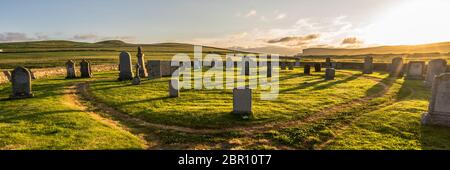 Panorama des alten Hügelgräberfriedhofs voller Grabsteine auf dem Shetland (Schottland, Großbritannien) bei einem magischen Sonnenuntergang mit dramatischem warmen Licht und einer grünen Wiese Stockfoto