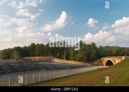 Ashokan Reservoir Überfluss mit Brücke, rollendes Gras, Bäume, blauer Himmel mit Wolken und Metallzaun in der goldenen Stunde. Stockfoto