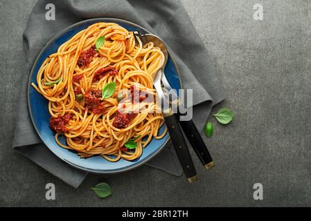 Köstliche Mahlzeit mit Spaghetti und Tomatensauce mit Basilikum auf grauem Hintergrund serviert. Stockfoto