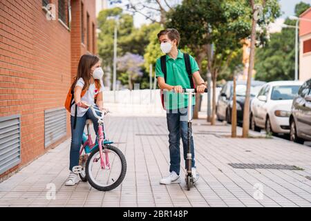 Junge und Mädchen tragen Masken und fahren einen Roller und Fahrrad auf der Straße Stockfoto