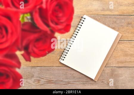 Draufsicht des leeren Blattes des Notizbuchs und der roten Rose auf rustikalem braunen Holztisch. Stockfoto