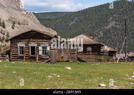 Alte verlassene Häuser in einem vergessenen russischen Dorf auf einem Hintergrund der Berge. Zerbrochene Fenster und kaputtes Dach. Stromleitungen. Grünes Gras und Steine auf dem Stockfoto