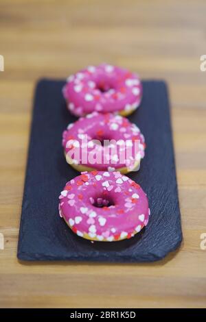 Drei rosa Donuts auf einem schwarzen Tablett Stockfoto