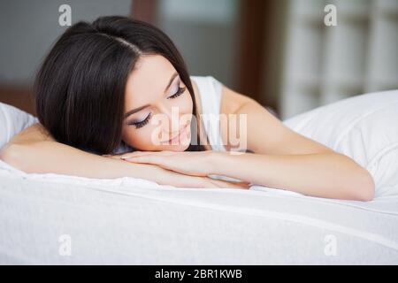 Guten Morgen. Porträt einer lächelnden, hübschen jungen Brunette-Frau, die sich im weißen Bett entspannen kann Stockfoto