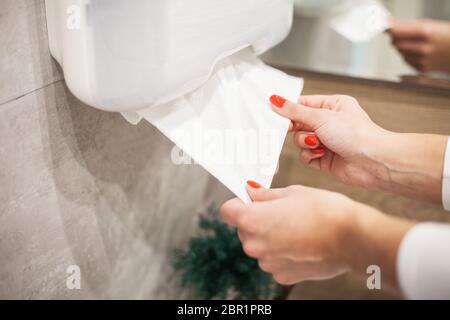 Spender für Papierhandtücher. Hand der Frau nimmt Papierhandtuch im Badezimmer Stockfoto