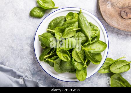 Baby-Spinat verlässt in der Schüssel auf grauem Betonhintergrund, Draufsicht, Kopierraum. Sauberes Essen, Entgiftung, Lebensmittelzutat Stockfoto