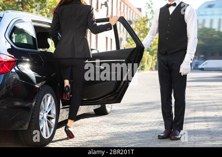 Männliche Valet Öffnen der Tür für die Geschäftsfrau, die sich aus einem Auto auf der Straße Stockfoto