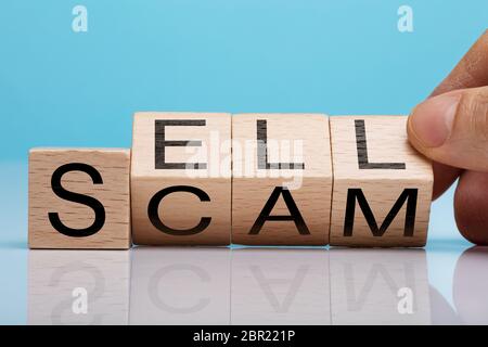 Des Menschen Hand mit Holzblock mit Verkaufen und Scam Text über reflektierende Schreibtisch Stockfoto