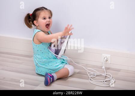 Niedliches Kleinkind Mädchen schreien Nach dem Berühren heißen Bügeleisen Eingesteckt. Rufen um Hilfe Stockfoto