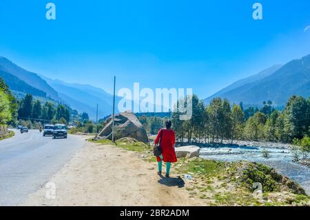 Eine Dame in rot Drees zu Fuß auf der Straße von einer Autobahn. Wunderschöne Landschaft panorama Shambhala-tal BIN ANALI - LEH-STRASSE, KULLU, JAMMU UND KAS Stockfoto