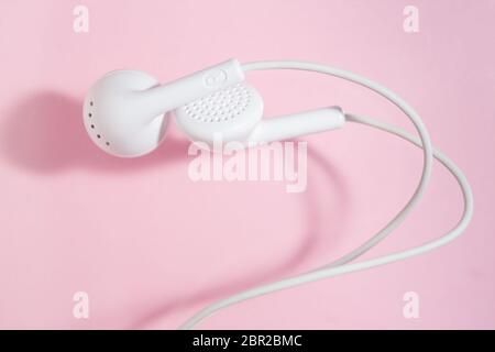 Weiße Ohrhörer auf hellem rosa Hintergrund. Geschlossene Ansicht von oben. Stockfoto