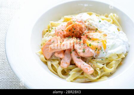 Fettucine mit Lachs, Ei und Parmesan, auf weiße Platte serviert. Stockfoto