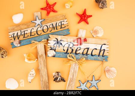 Holzschilder begrüßen Strand, Seesterne und Muscheln auf gelbem Hintergrund. Stockfoto