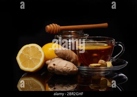 Honig im Glas Kanne und Tasse Tee mit Ingwer und Zitrone auf einem schwarzen Hintergrund. Stockfoto