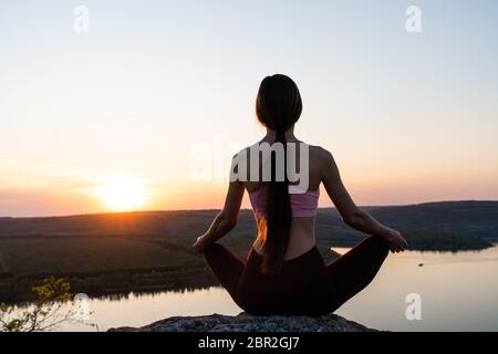 Blick auf junge Frau Yoga bei Sonnenaufgang am See, Menschen Meditation Gelassenheit Konzept und Wohlbefinden im Leben, Lotus Yoga Position Stockfoto