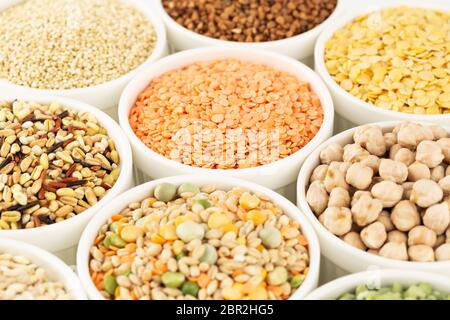 Die Kollektion von verschiedenen Leisten in den weißen Keramikschalen. Erbsen teilen, Linsen bunt, Buchweizen, Kichererbsen, Weizenkörner, Quinoa. Stockfoto