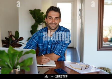 Lächelnder junger Mann, der von zu Hause aus in seinem Wohnzimmer arbeitet Stockfoto