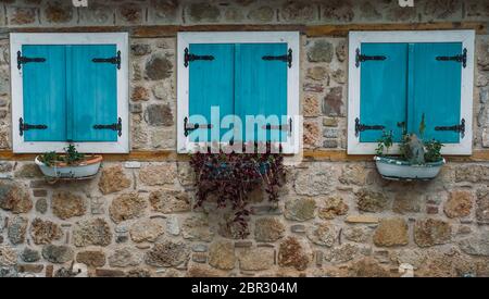 Antalya, Türkei - 7. Mai 2020: Drei Fenster an der Steinwand mit türkisfarbenen Holzjalousien und Töpfen, die vor dem Hotel hängen Stockfoto