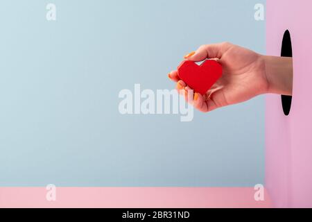 Die Hand der Frau hält ein rotes Papierherz auf blauem und rosa Hintergrund Stockfoto