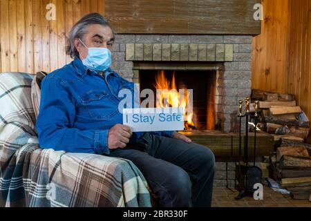 Covid-19 Coronavirus. Konzept für den Aufenthalt zu Hause. Ein älterer Mann in einer schützenden medizinischen Maske sitzt vor dem Kamin. Stockfoto