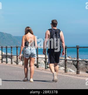 Ein junges Paar schlendert entlang der Esplanade in Sidmouth und genießt den heißen Sonnenschein vor dem Feiertagswochenende. Quelle: DWR/Alamy Live News Stockfoto