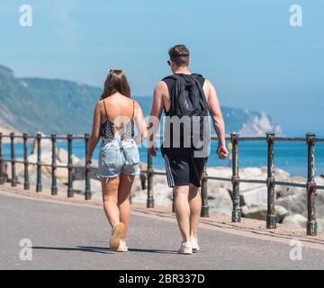 Ein junges Paar schlendert entlang der Esplanade in Sidmouth und genießt den heißen Sonnenschein vor dem Feiertagswochenende. Quelle: DWR/Alamy Live News Stockfoto