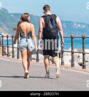 Ein junges Paar schlendert entlang der Esplanade in Sidmouth und genießt den heißen Sonnenschein vor dem Feiertagswochenende. Quelle: DWR/Alamy Live News Stockfoto