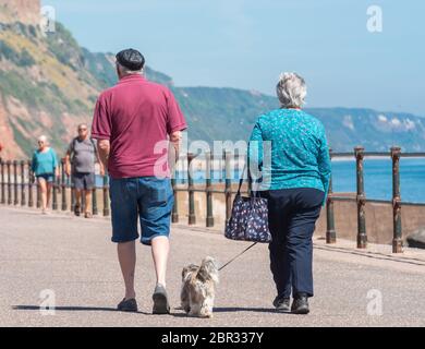 Ein Paar schlendern entlang der Esplanade in Sidmouth und genießen die heiße Sonne vor dem Feiertagswochenende. Quelle: DWR/Alamy Live News Stockfoto